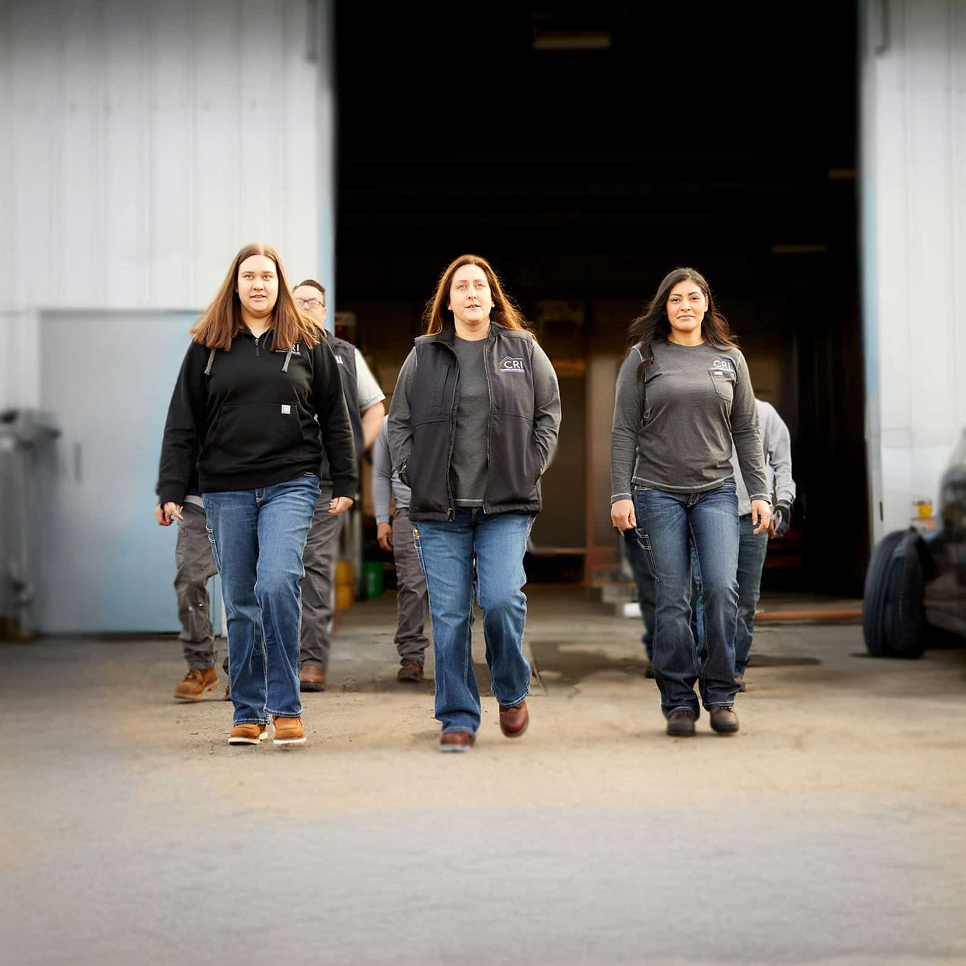 Three women in workwear walking out of a shop, wearing safety footwear