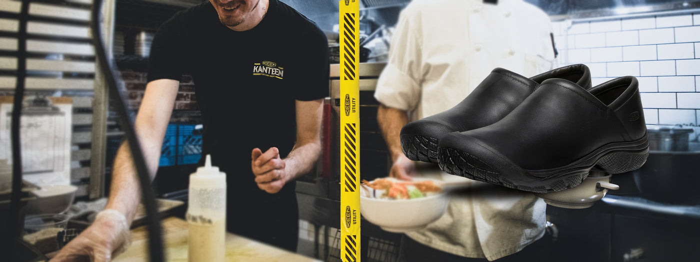Black slip-resistant work clogs in a commercial kitchen with chefs working in the background.