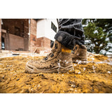 A close-up of a person wearing a pair of muddy DEWALT work boots standing on wet, splashing dirt outdoors
